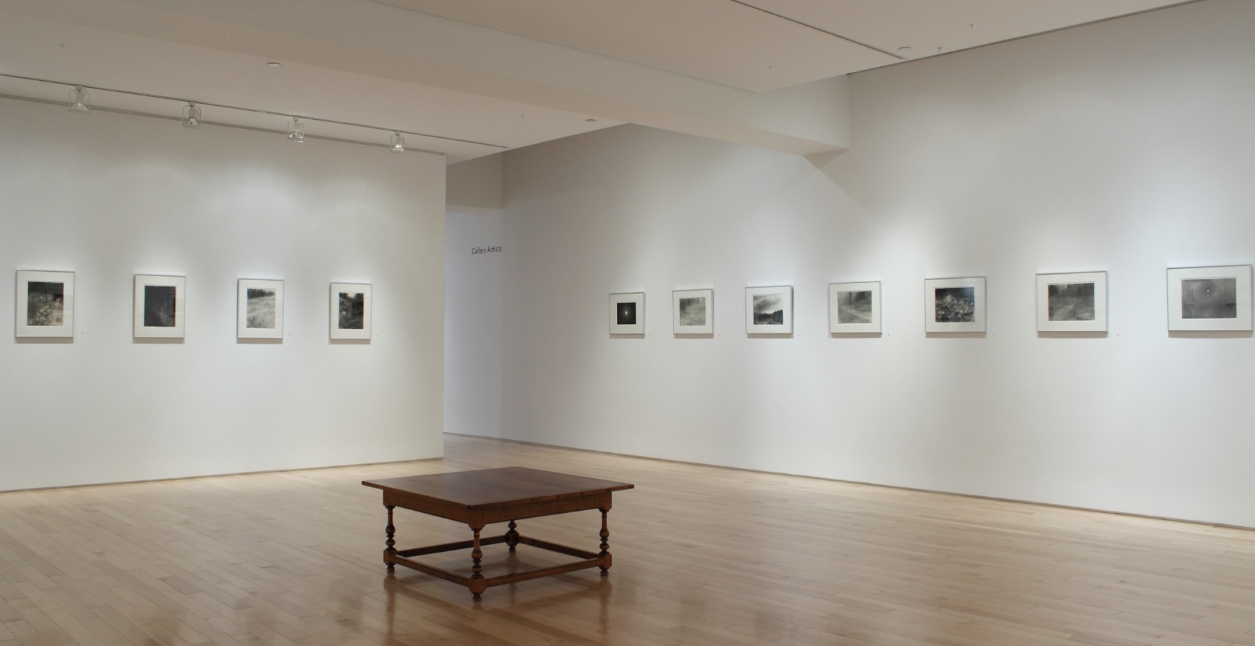 Photograph showing a corner view of an exhibition space, with eleven framed drawings hanging on white walls