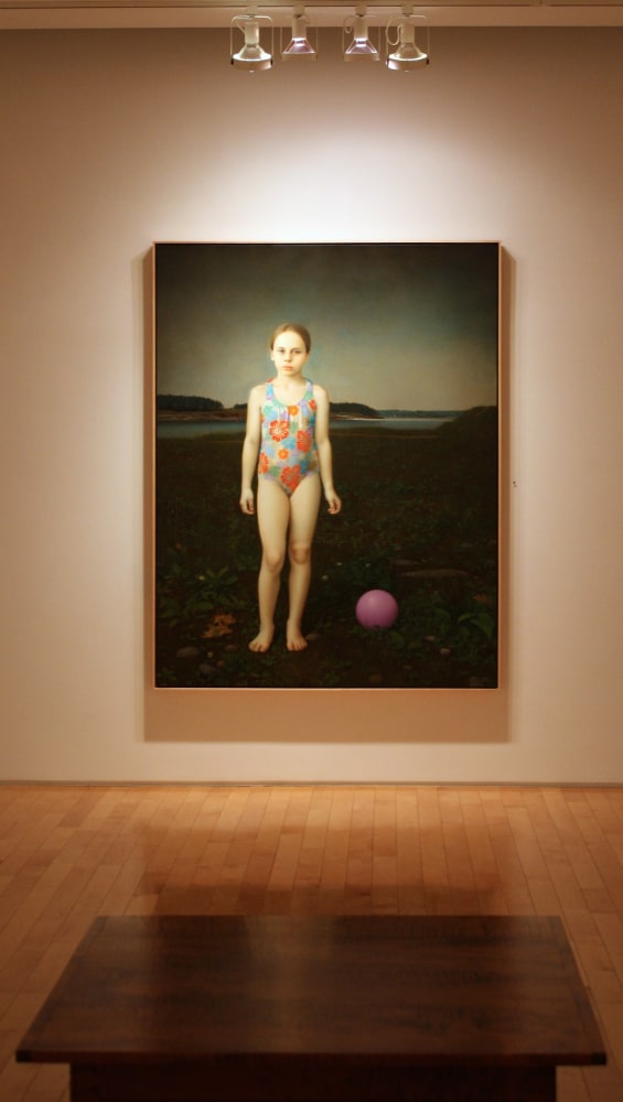 Photograph showing a view of an exhibition space, with one large framed painting hanging on a white wall