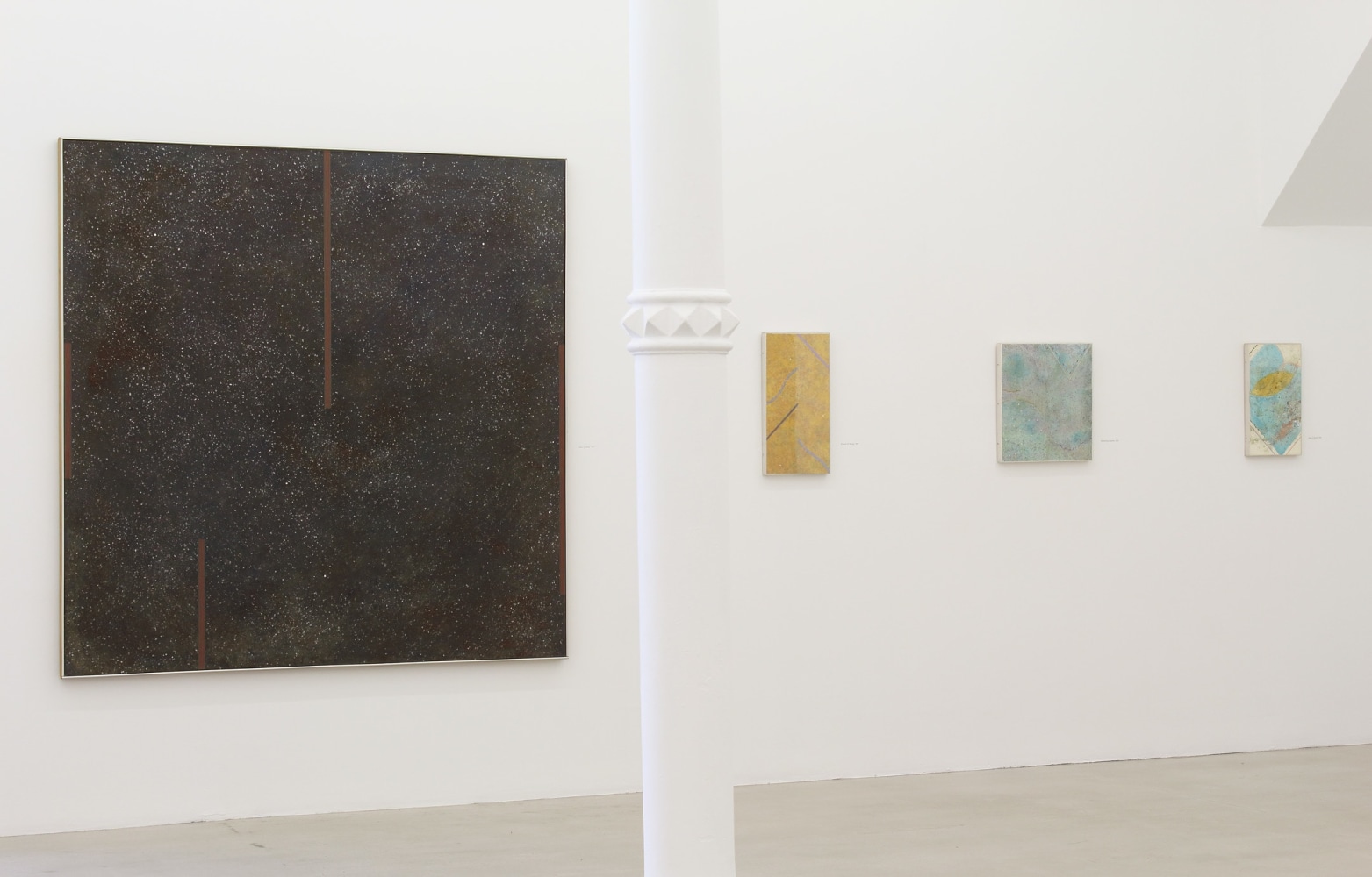 Photograph showing a view of an exhibition space, with four paintings hanging on a white wall