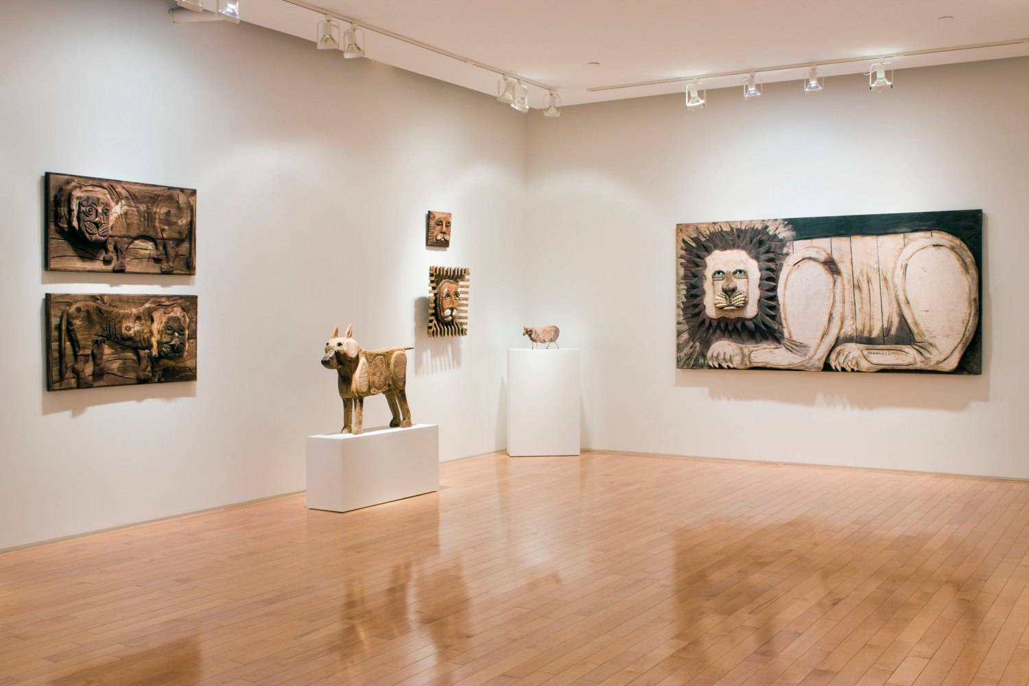 Photograph showing a corner view of an exhibition space, with five sculptures hanging on the walls and two sculptures on pedestals