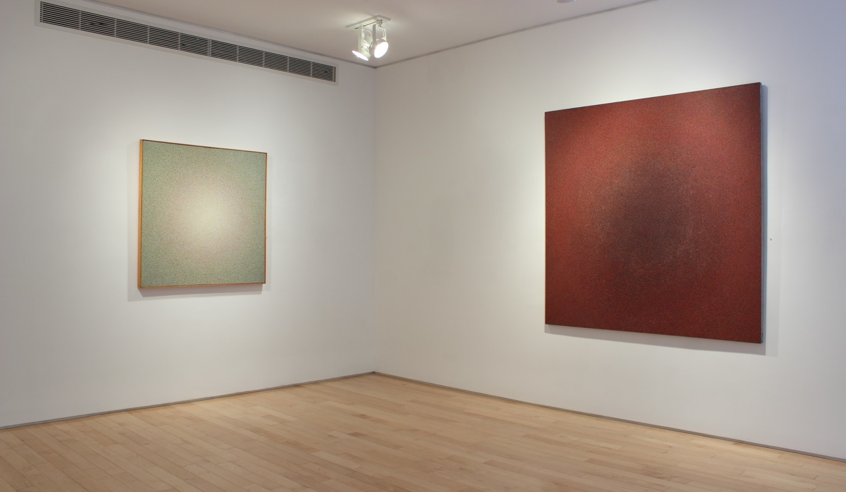 Photograph showing a corner view of an exhibition space, with two paintings hanging on the white walls