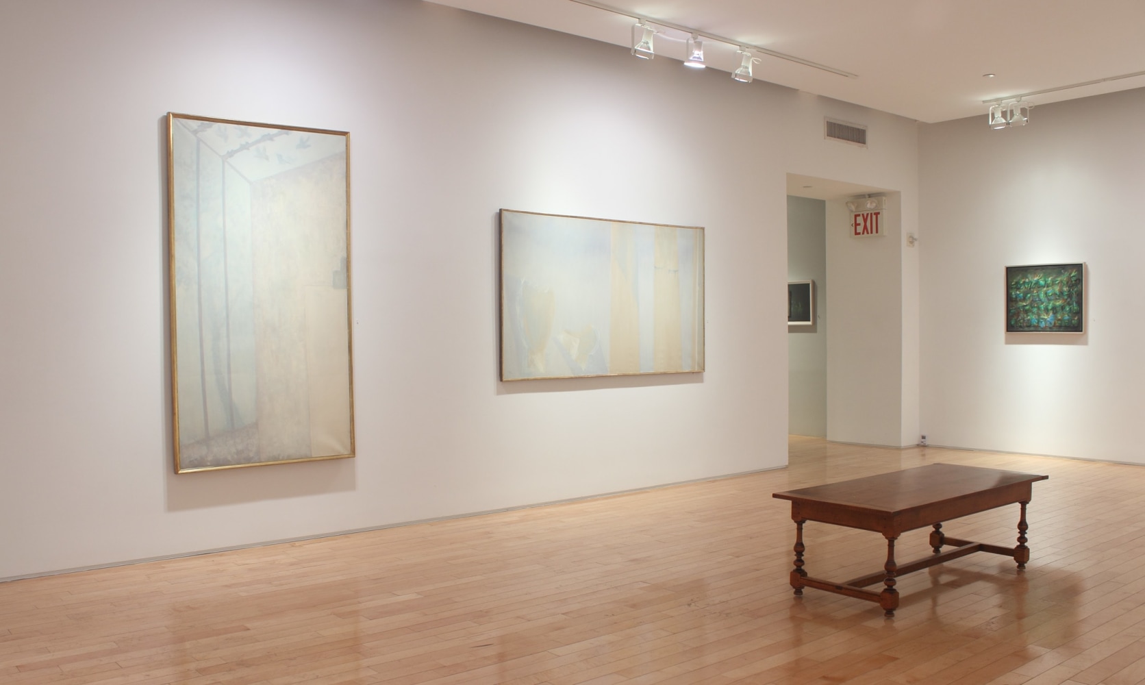 Photograph showing a corner view of an exhibition space, with two large paintings and one smaller painting hanging on white walls