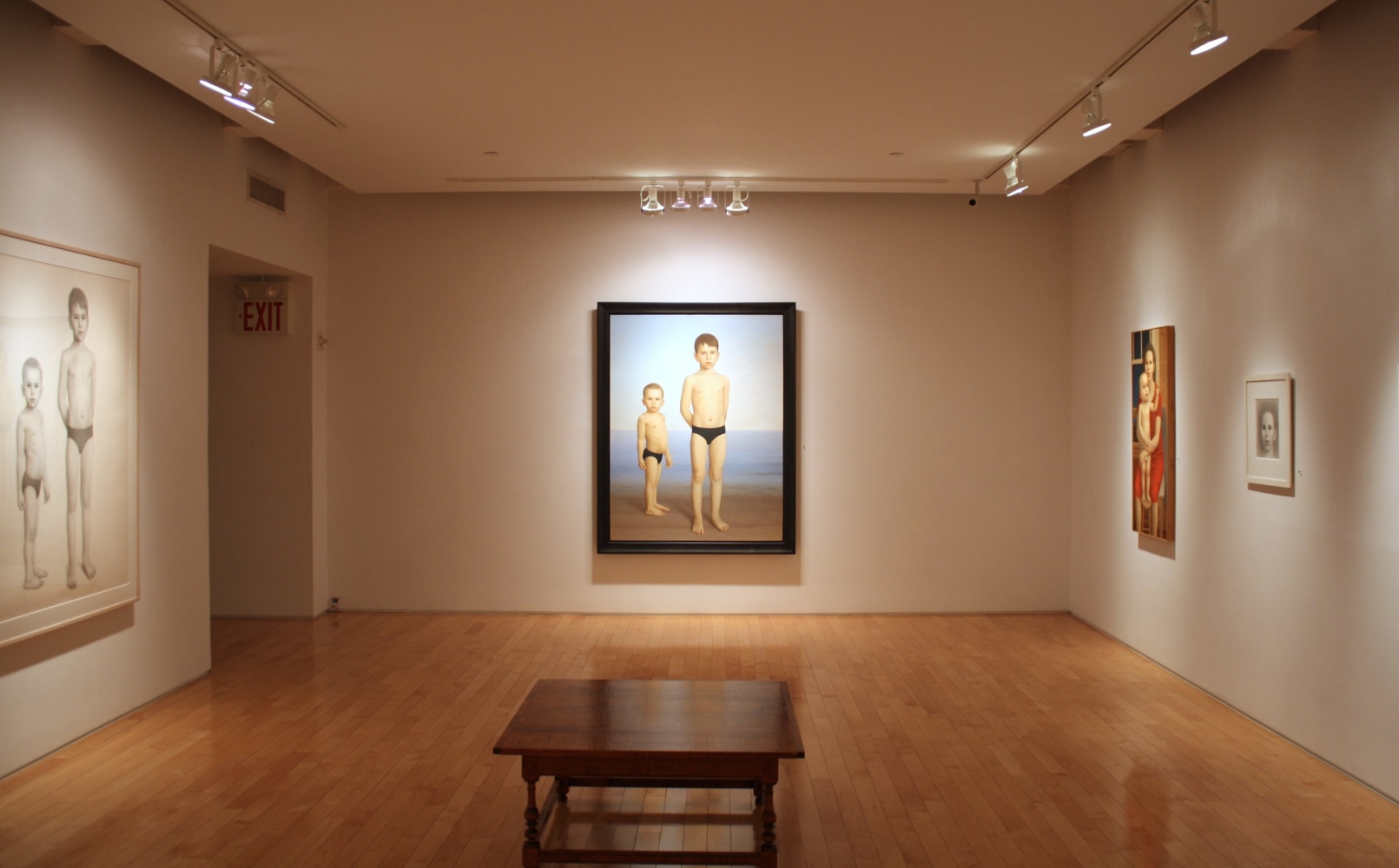 Photograph showing a corner view of an exhibition space, with two large framed paintings, a large framed drawing and a small framed drawing hanging on white walls