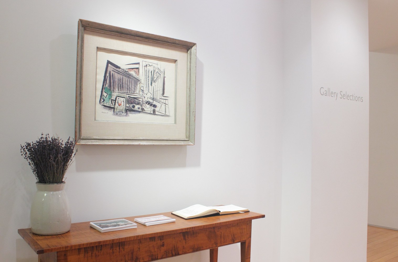 Photograph showing a view of an exhibition space, with a framed painting hanging over a wooden table, and wall text that reads &quot;Gallery Selections&quot; to the right