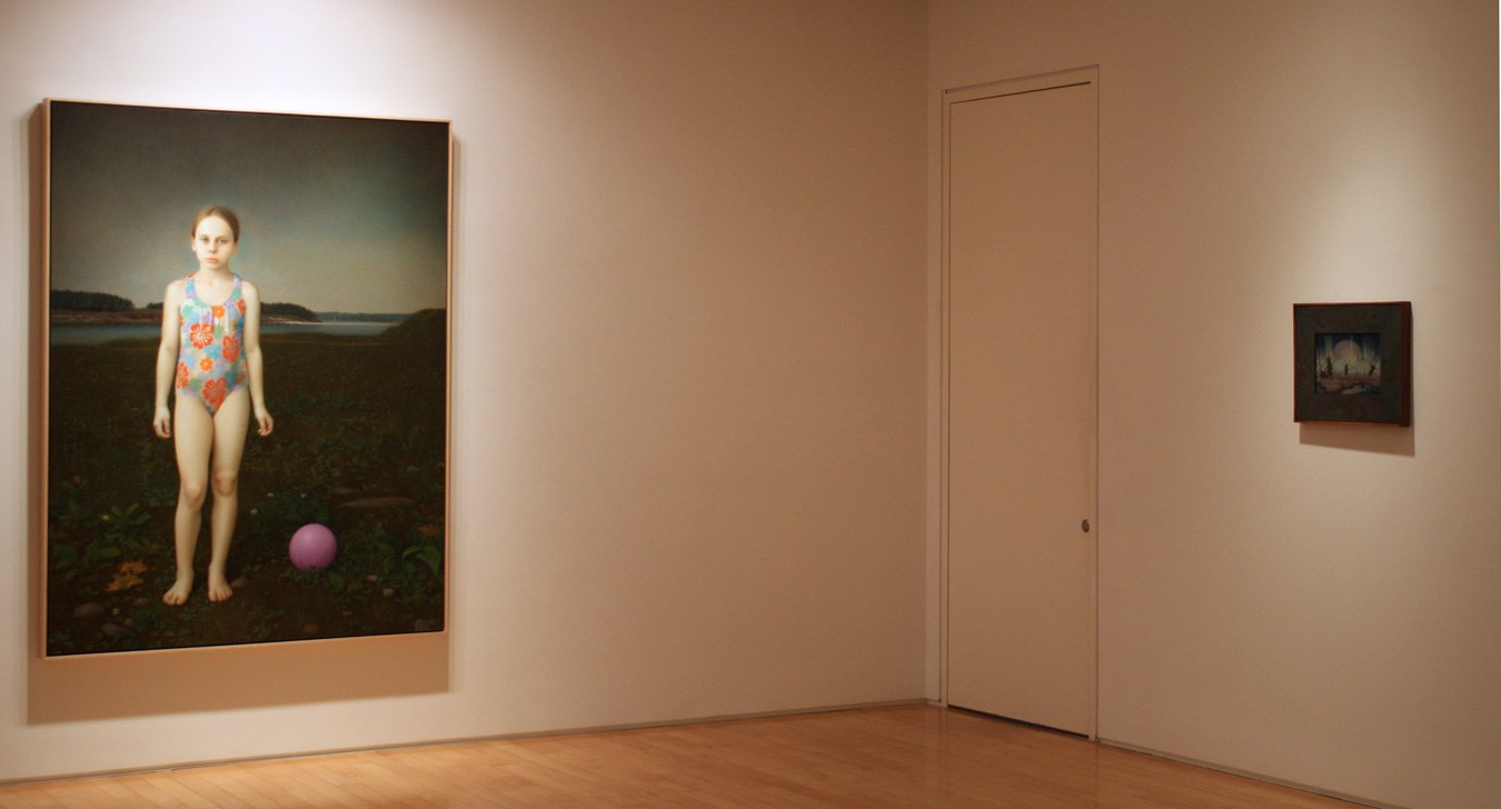 Photograph showing a corner view of an exhibition space, with two framed paintings hanging on white walls