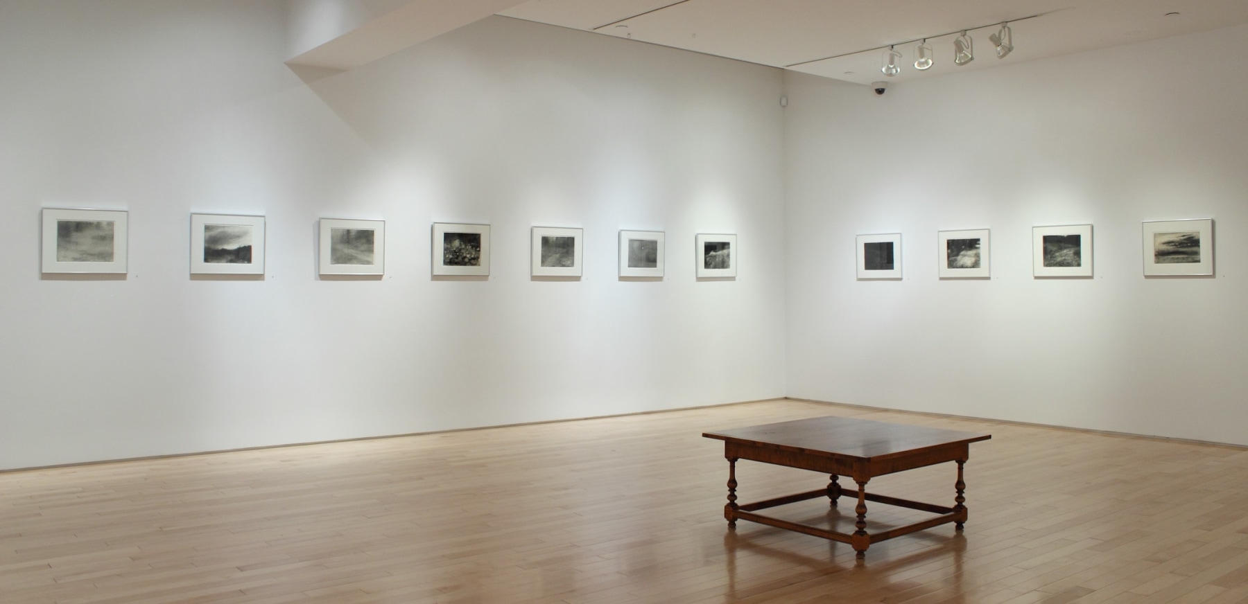 Photograph showing a corner view of an exhibition space, with eleven framed drawings hanging on white walls