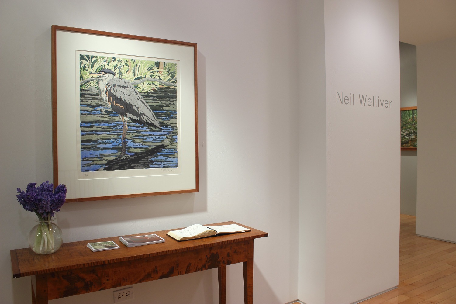 Photograph showing a view of an exhibition space with a framed drawing hanging on a wall over a wooden table