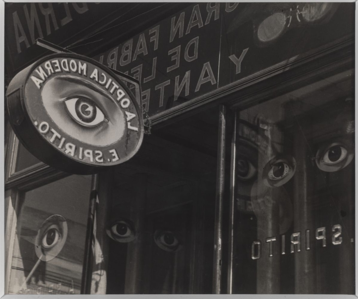 The images of graphic eyes are shown reflecting on the windows of an optometrist storefront and sign.