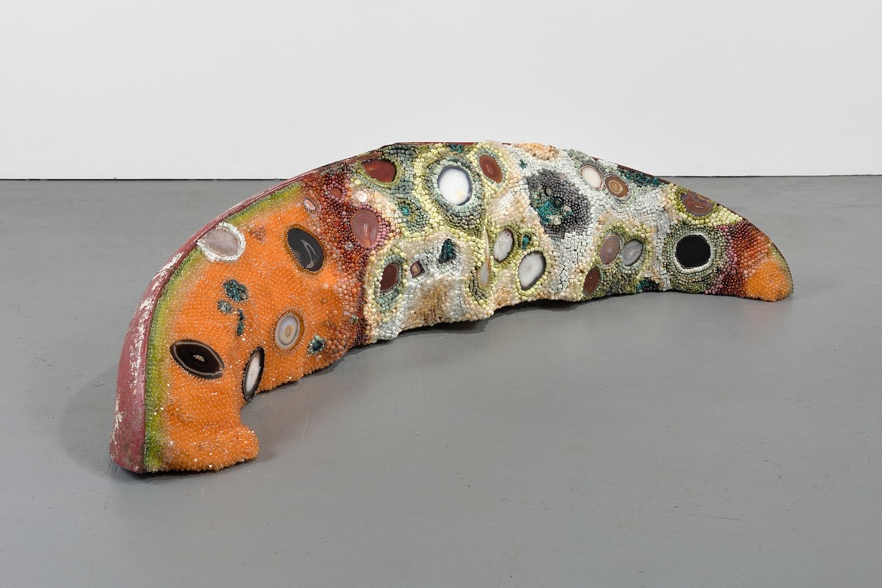 Kathleen Ryan's sculpture Bad Melon (Rainbow) from 2022, made from beads of Calcite, serpentine, prehnite, rhodonite, amazonite, aquamarine, onyx, jasper, ruby in zoisite, turquoise, labradorite, rose quartz, agate, carnelian, magnesite, marble, acrylic, steel pins on coated polystyrene, Volkswagen hood; with dimensions of 21.5&quot; H x 90&quot; L x 29&quot; W