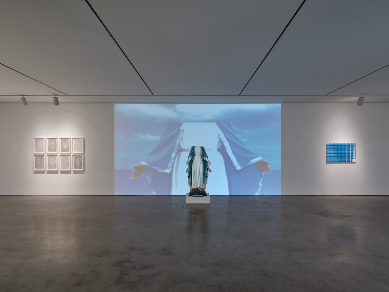 Installation view of &quot;Laura Anderson Barbata: Singing Leaf&quot; showcasing a headless Virgin Mary in front of a projector screen.