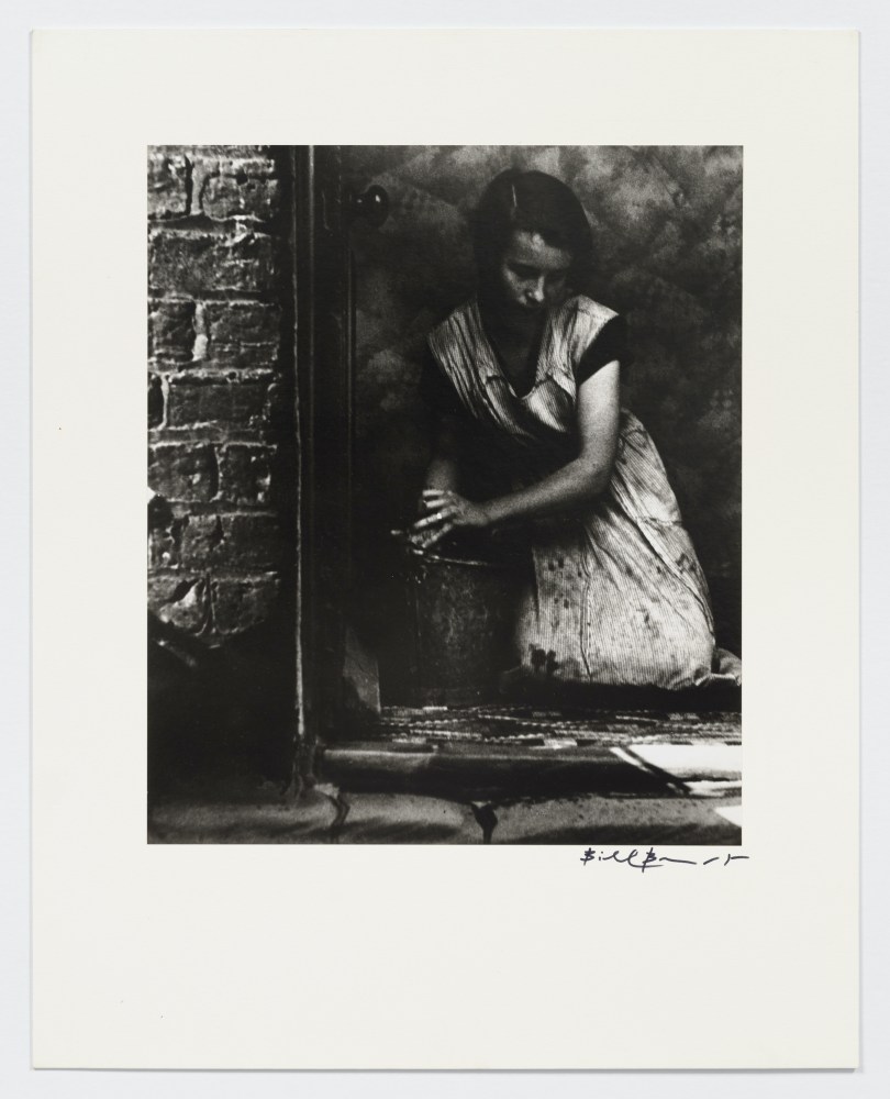 Black and white photographic portrait of a young housewife cleaning ground with bucket of water.