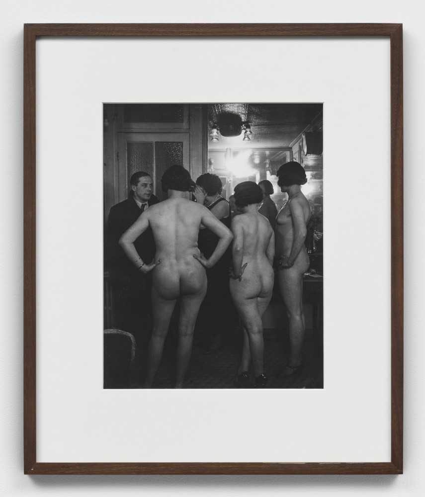 Black and white photographic portrait of three nude women standing before a man at Suzy's.