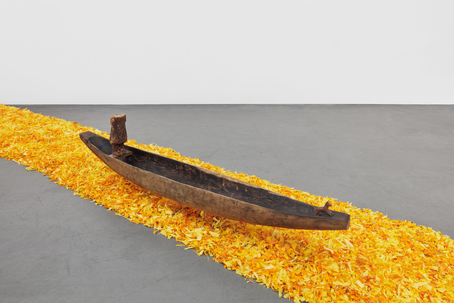 A wooden canoe with a headless figure made of corn and a small wax dog floats above a river of marigolds.