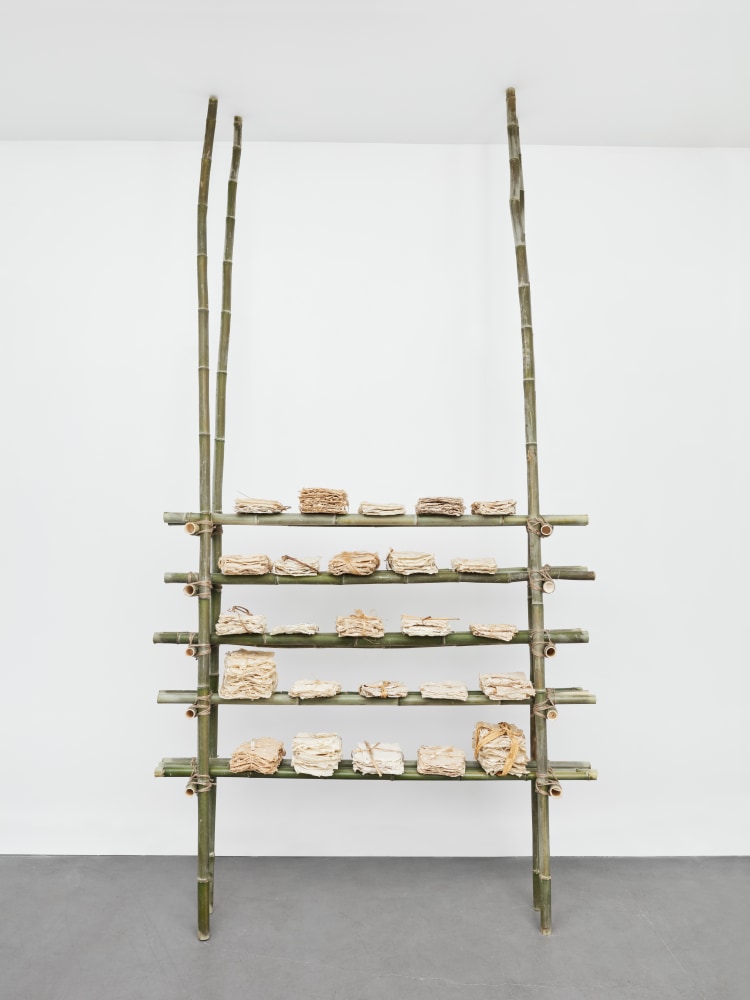 A green bookshelf made of bamboo holds several bound paper bundles.