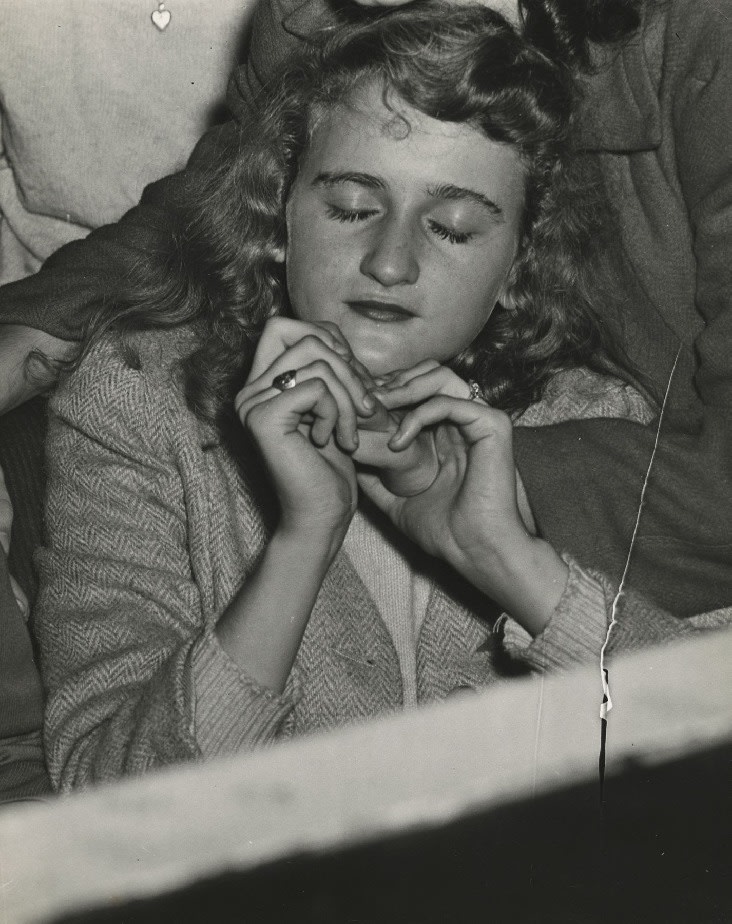A black and white photographic print by Weegee of a girl at the Palace Theatre with her eyes closed listening to Frank Sinatra