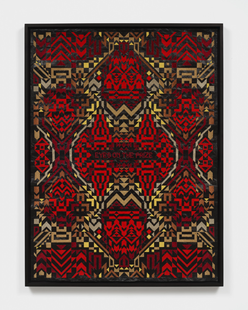 A framed artwork with red and yellow embroidered patterns on black roofing material with &quot;Eyes on the Prize&quot; in the center.