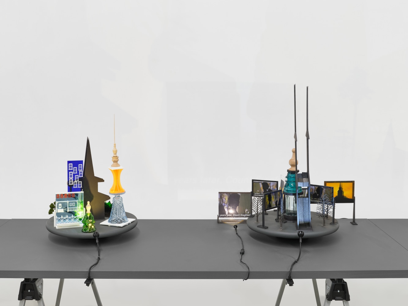 A series of assemblage sculptures comprised of upside down crystal vases, miniature street lamps, photographs printed on plexiglass and steeples made from styrene atop rotating platforms.