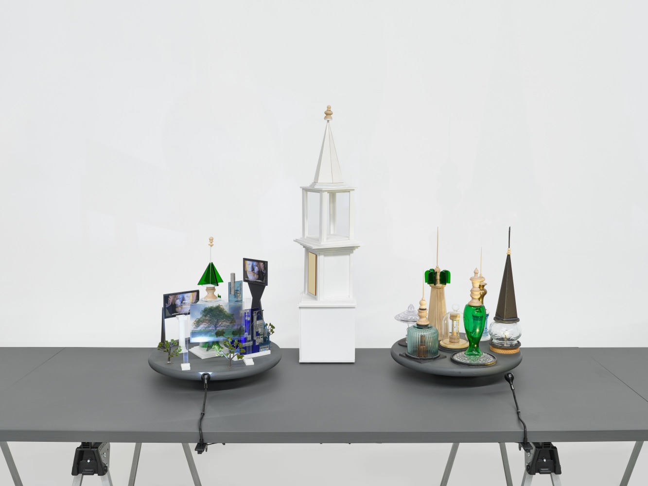 A series of assemblage sculptures comprised of upside down crystal vases, miniature street lamps, photographs printed on plexiglass and steeples made from styrene atop rotating platforms.