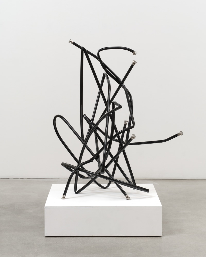 A freestanding sculpture by Josh Callaghan of black metal tubing with chair leg caps entangled and extending in all directions.