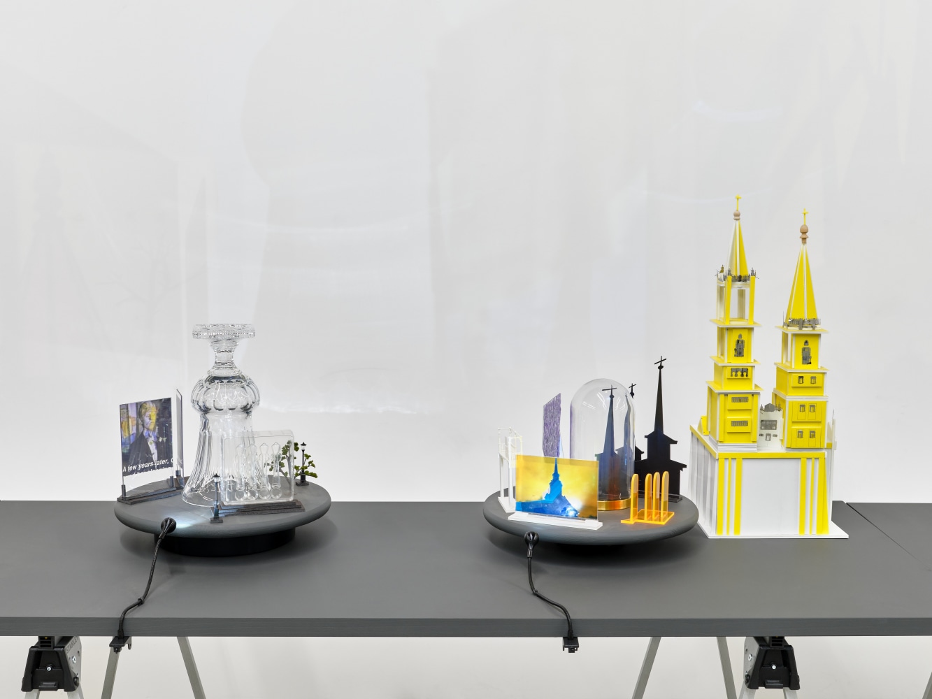 A series of assemblage sculptures comprised of upside down crystal vases, miniature street lamps, photographs printed on plexiglass and steeples made from styrene atop rotating platforms.