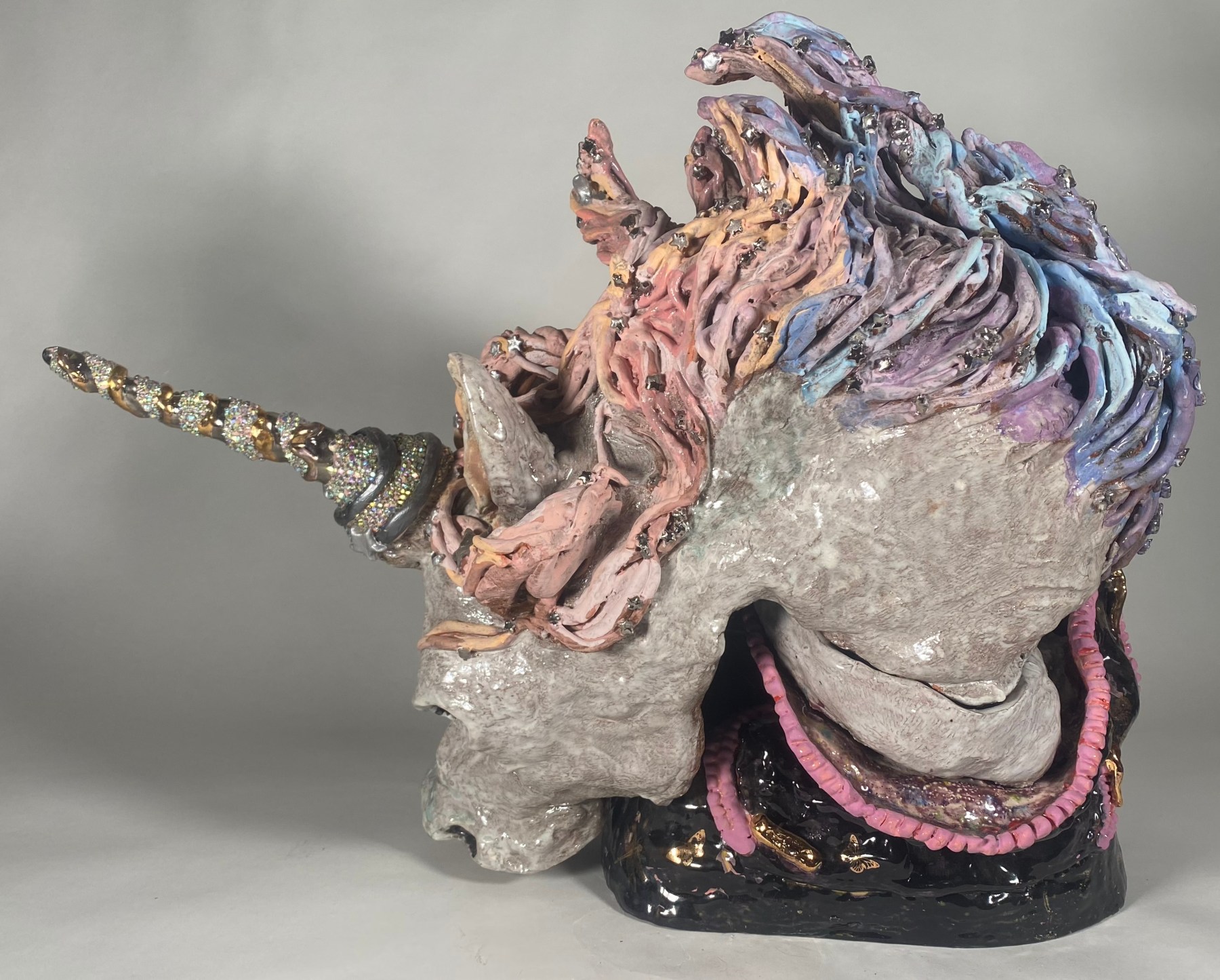 A grey unicorn sculpture with a pink and purple mane and glittering horn, all made from stoneware, epoxy, and glass.