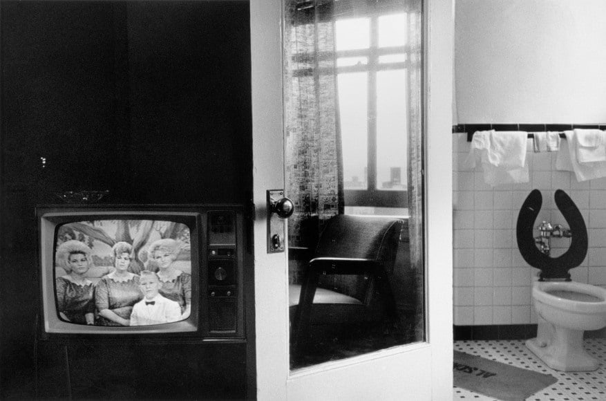 Black and white photo of a hotel room with television, door and toilet