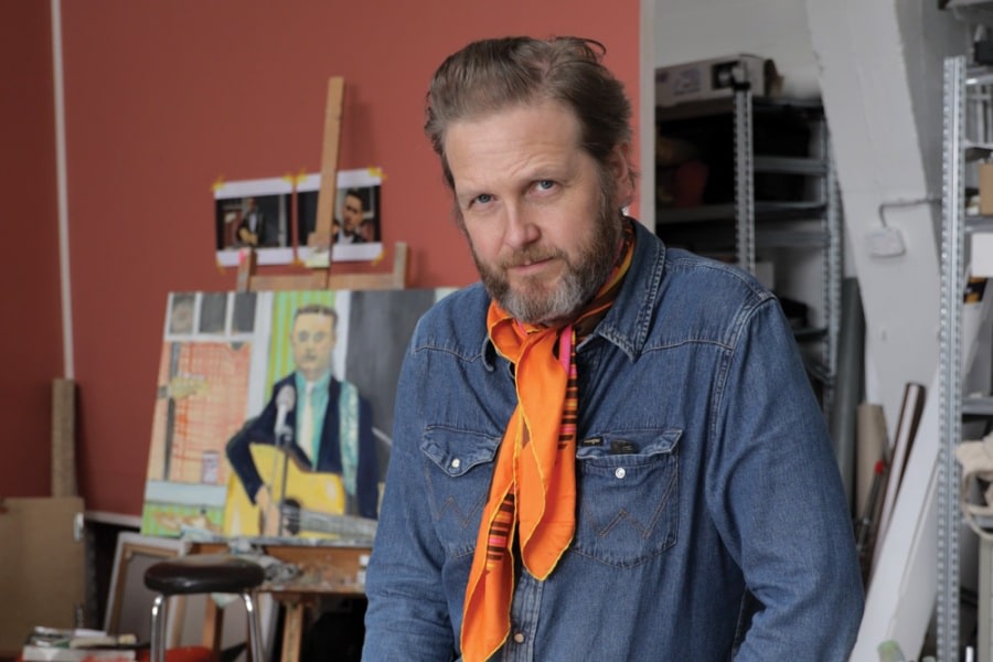 Portrait of an artist in his studio, wearing denim shirt and orange scarf