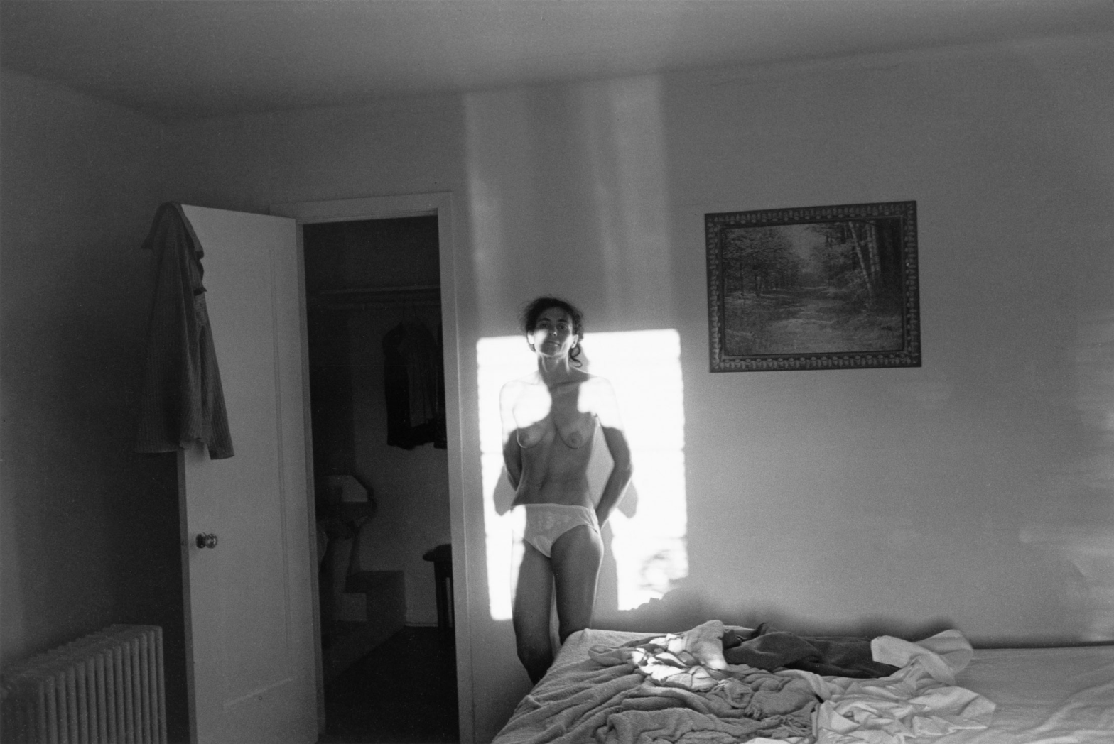 Black and white photo of a nude woman framed by a window's light in a hotel room