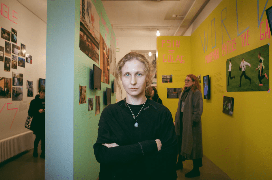 Woman standing in front of an art gallery installation of many pictures and photographs hung salon-style