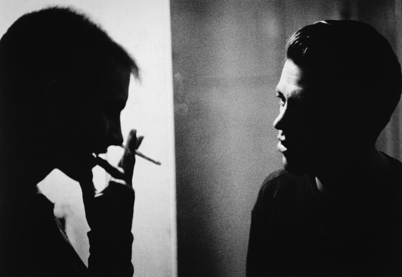 Black and white photograph of 2 men in conversation in a dark room