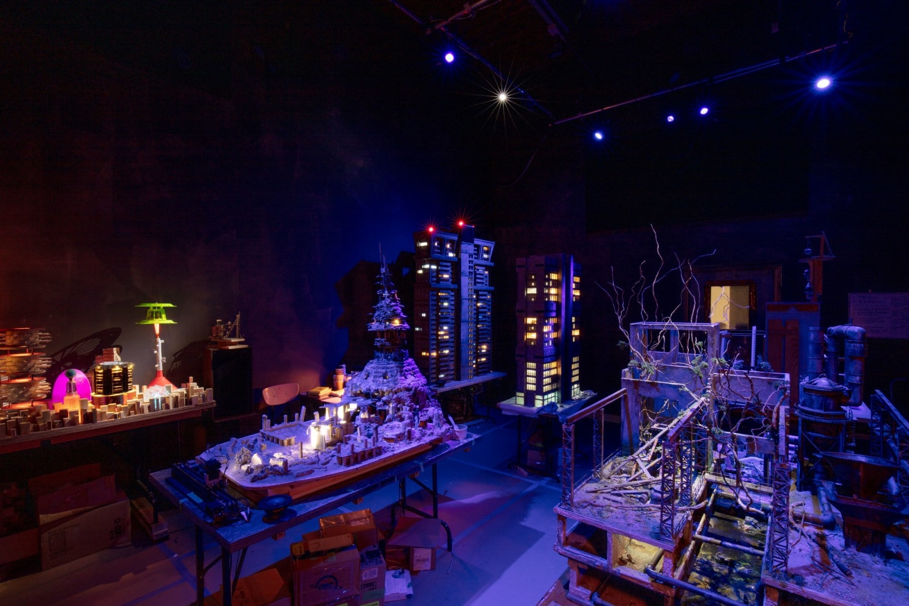 Gallery installation of a miniature city bathed in dark blue light