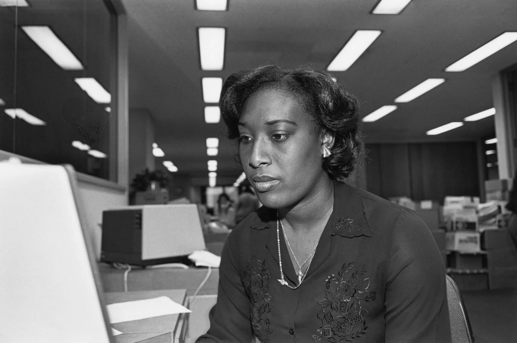 Black and white photograph of a woman sitting in front of a computer in an office, circa 1986