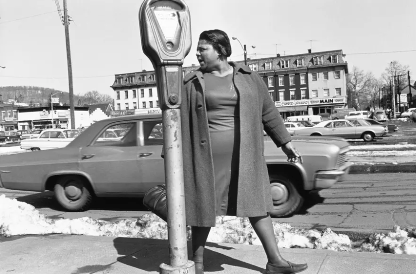 Black and white photograph of a middle aged woman looking behind her as she walks down a street in the 1960s