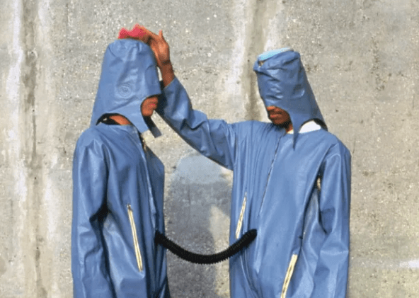 Two people wearing light blue jumpsuits and hoods as part of an artwork