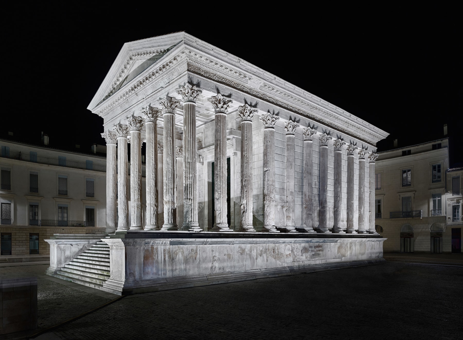 Nighttime photo of a dramatically lit classical Greco Roman building in Nimes, France.