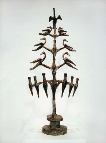 Decorative tall menorah with candle holders placed in a row toward the base, and a number of flying birds in two columns above.
