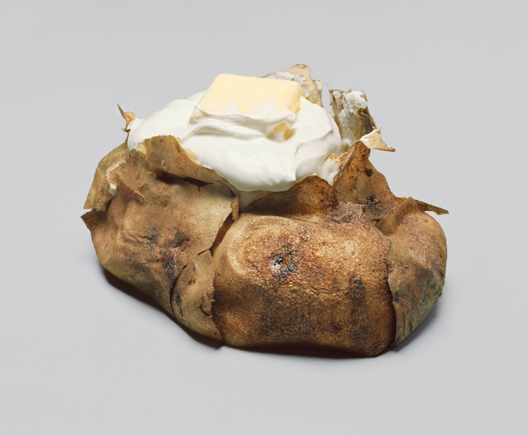 Oversized baked potato with sour cream and butter based on Claes Oldenburg sculpture. Presented as a photograph.