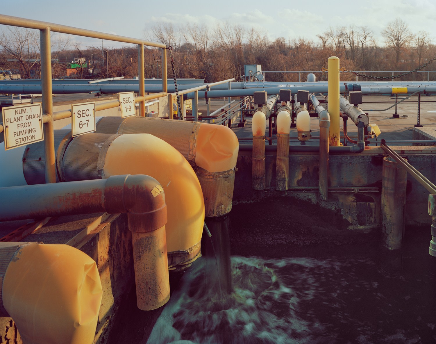 Influent, Sec. 6-7, 1-9, Photograph of a water treatment plant, water selling from orange pipes, grey and orange handrails, numerical signs