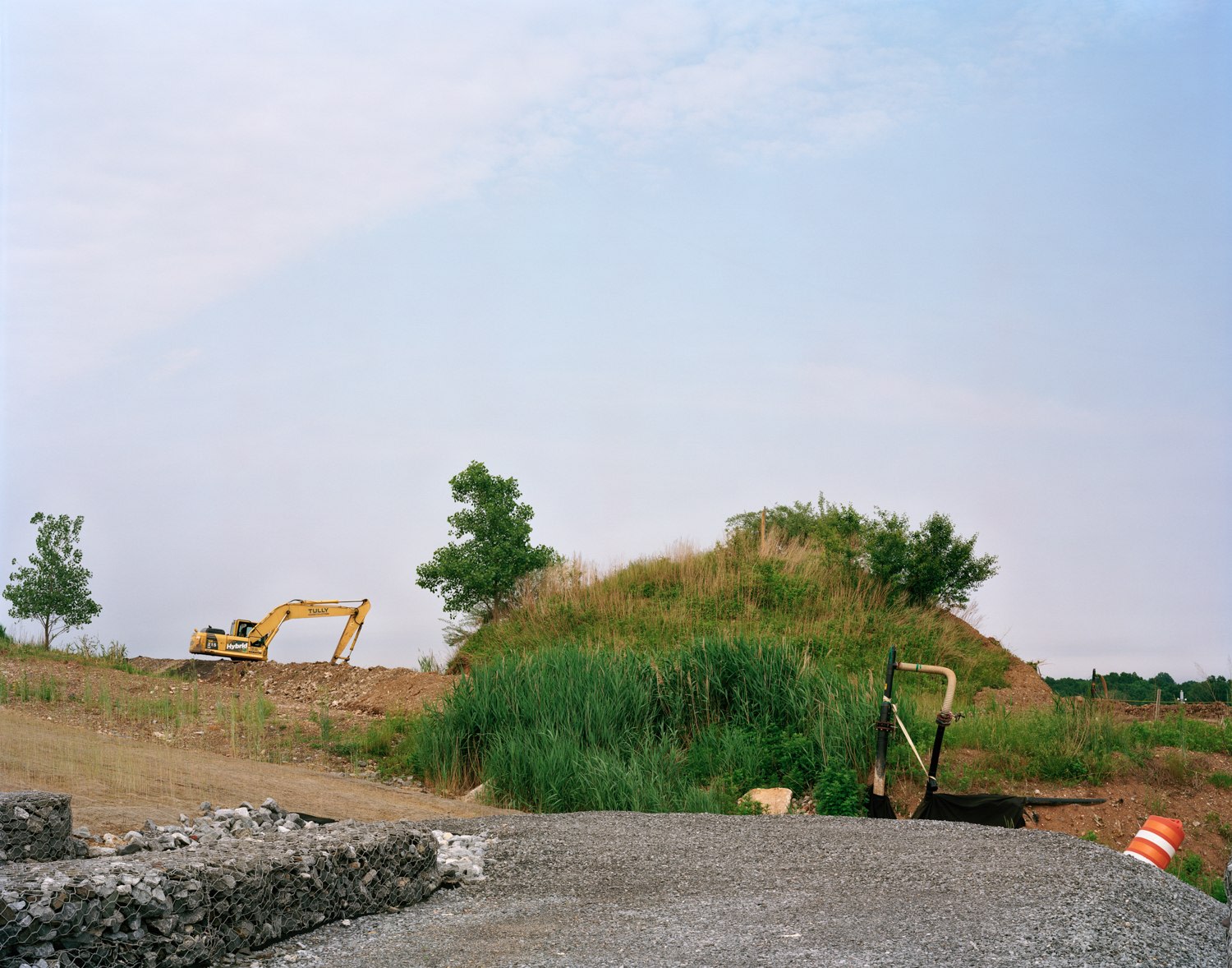 Old Landscape with New Interior Road and Gabion Wall, West Mound, 2019, Photograph of a mound of old landscaping, along a new road with big digger and other construction machinery in the distance, West Mound, Freshkills, NYC