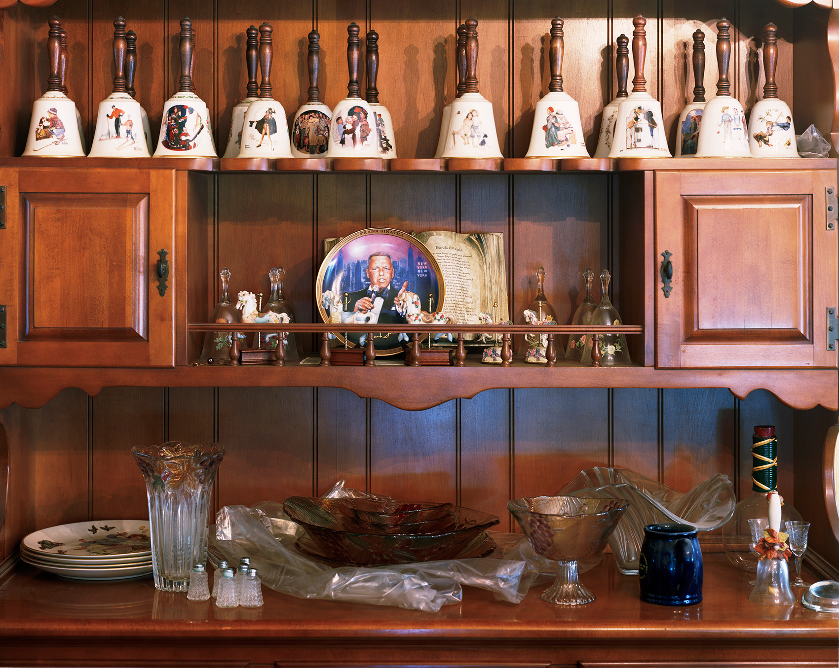 Photograph of old fashion china cabinet with row of bells, by Jade Doskow