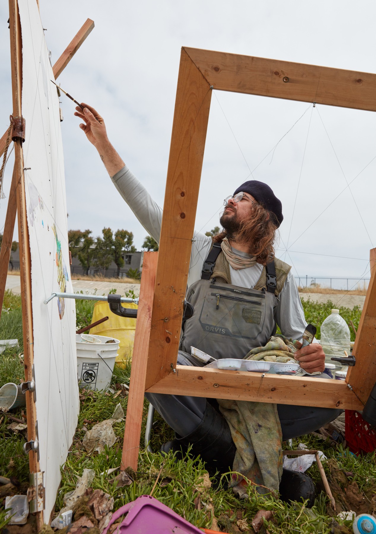 A photograph of Sterling Wells painting in the garbage strewn grass on the shores of Ballona Creek. 
