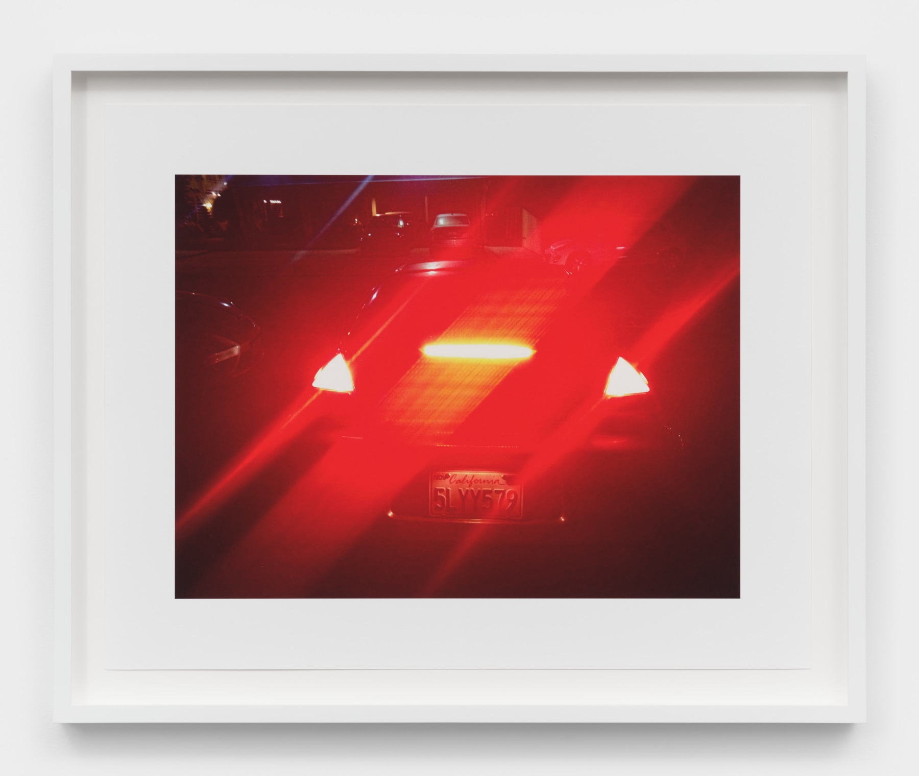 A photograph of a car with its rear brake lights engaged and refracting across the image. 
