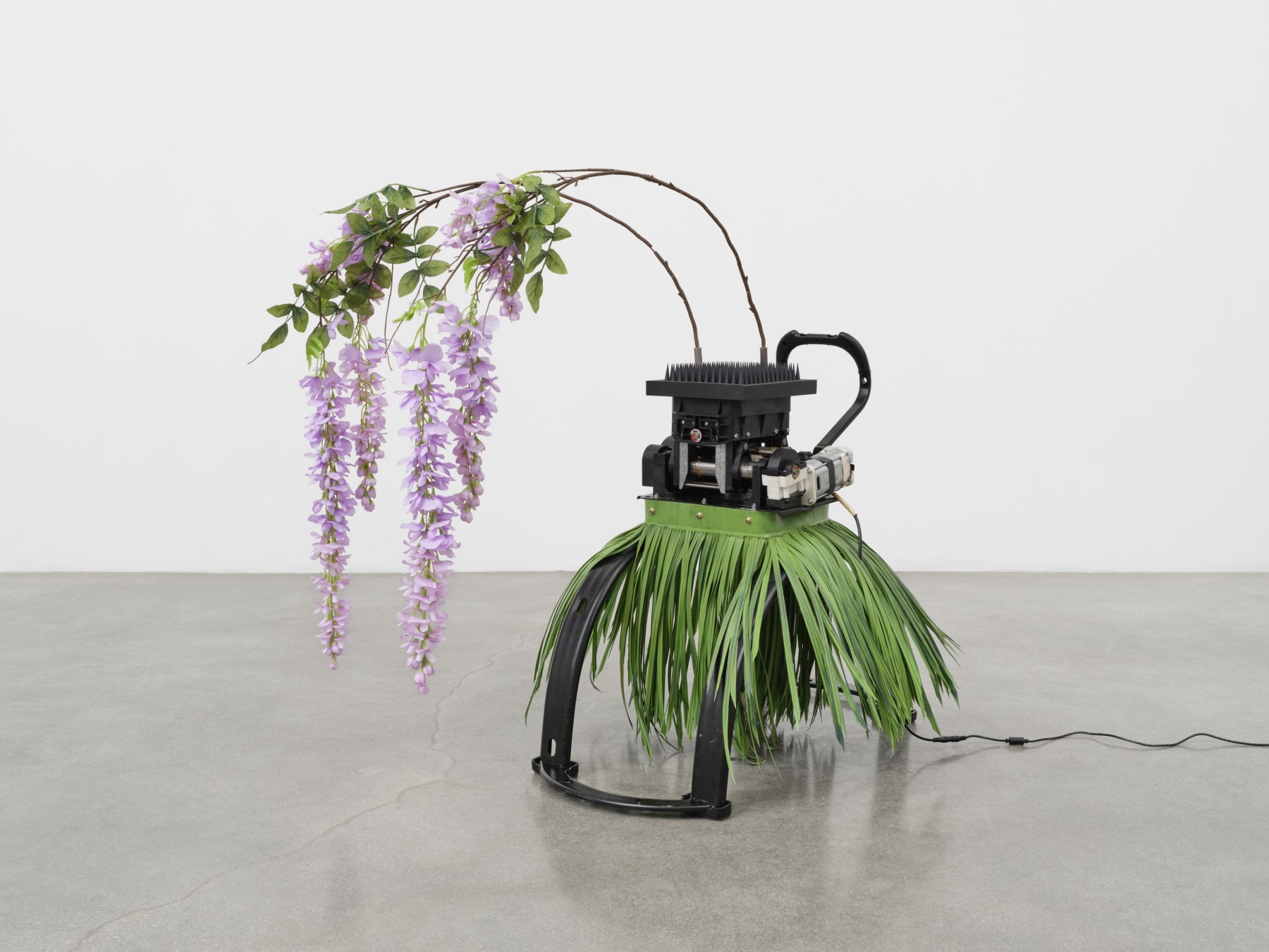 A sculpture by Rachel Youn titled "Ceremony," 2023, featuring a riding exercise simulator, wood, steel, plastic spikes, and artificial plants