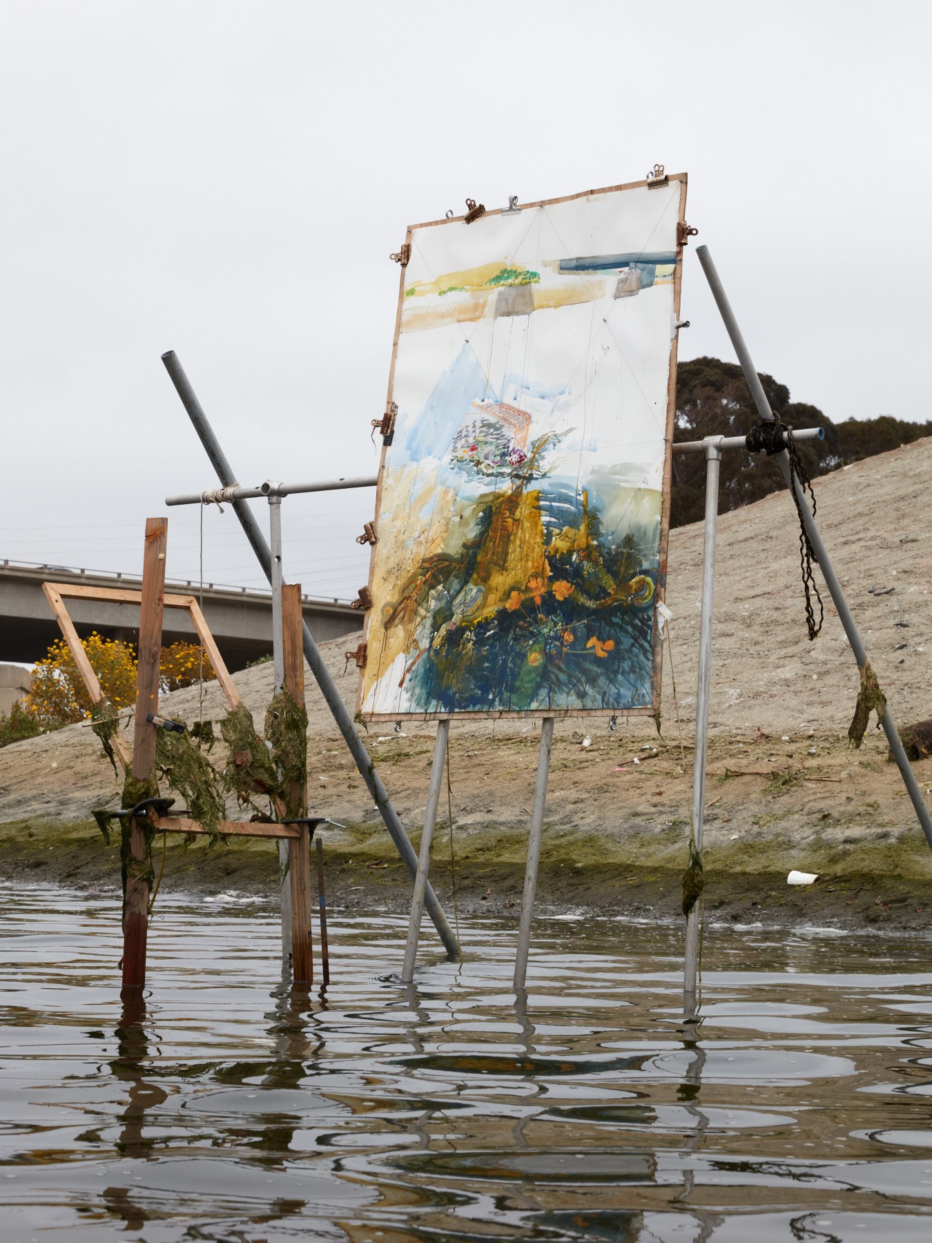 An easel made of metal poles and wood anchored in the Ballona Creek holds Sterling Wells' "Shopping Carts and Poppies" in progress. 