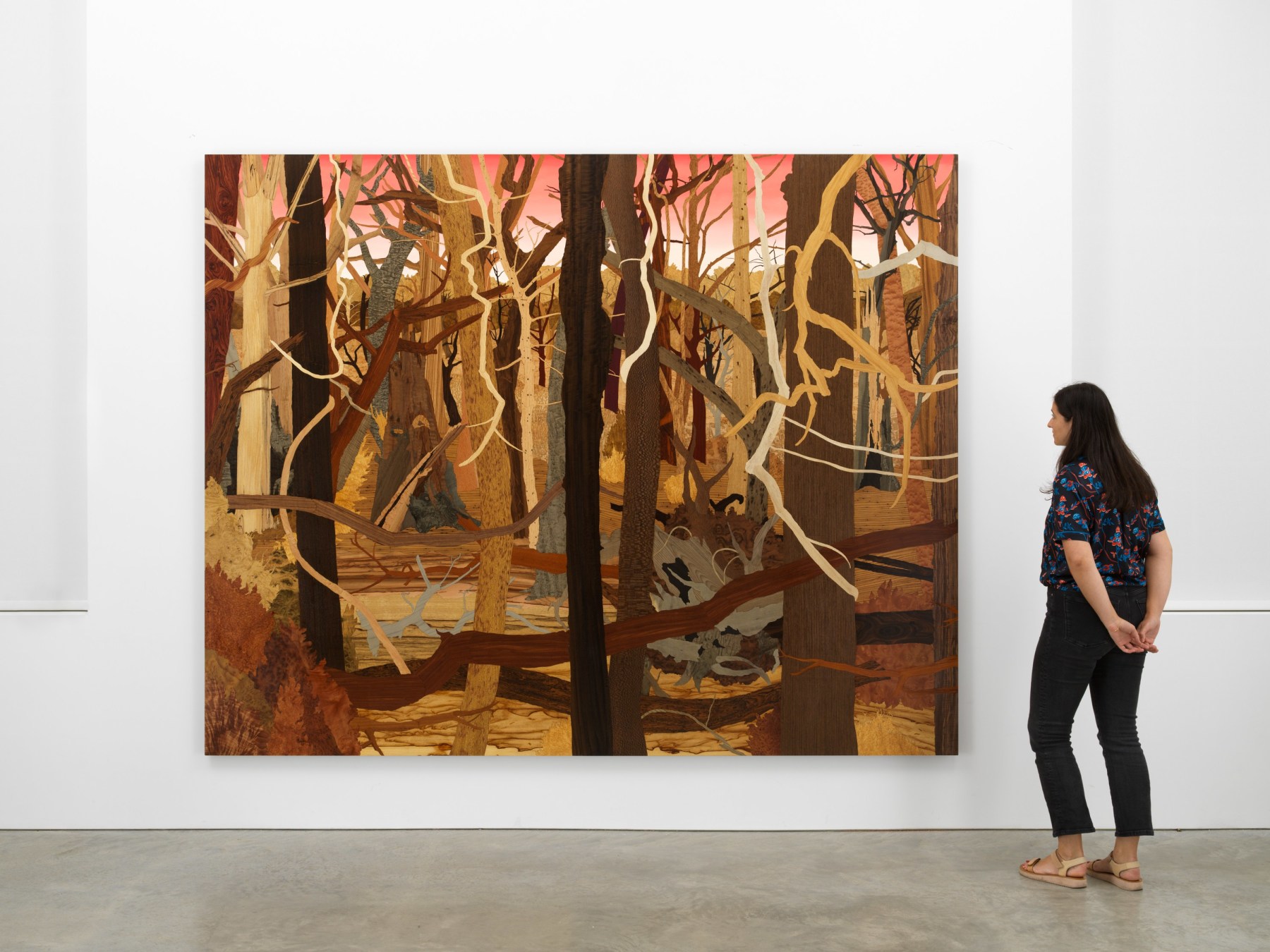 woman staring at an artwork depicting a forest of dead trees and branches
