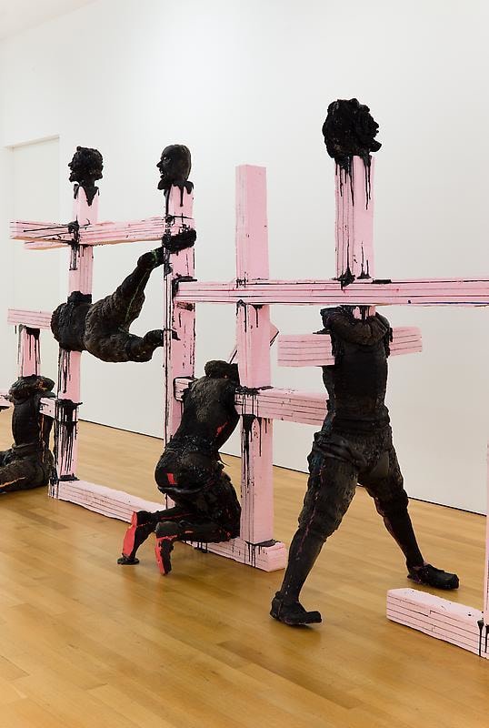 sculpture of bodies covered in black paint with pink beams protruding from them