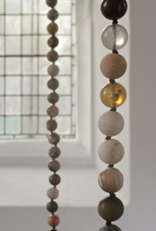 close up of a necklace suspended in mid-air composed of brown, grey, and white beads