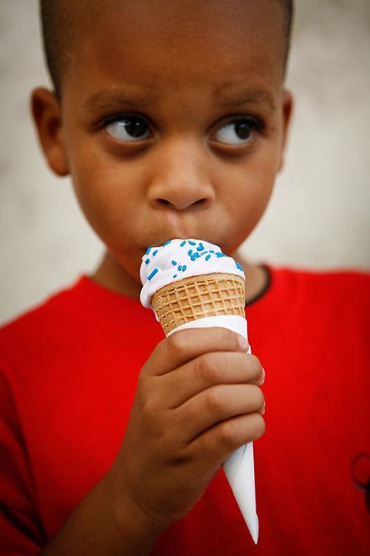 child wearing a red shirt eating vanilla soft serve with blue sprinkles on a waffle cone
