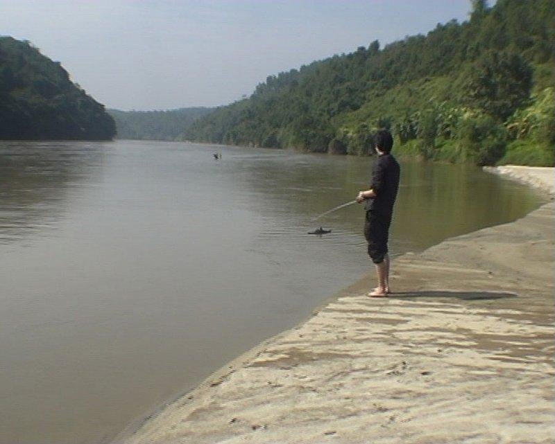 video still showing a person, barefoot, fishing in a body of water within a forest