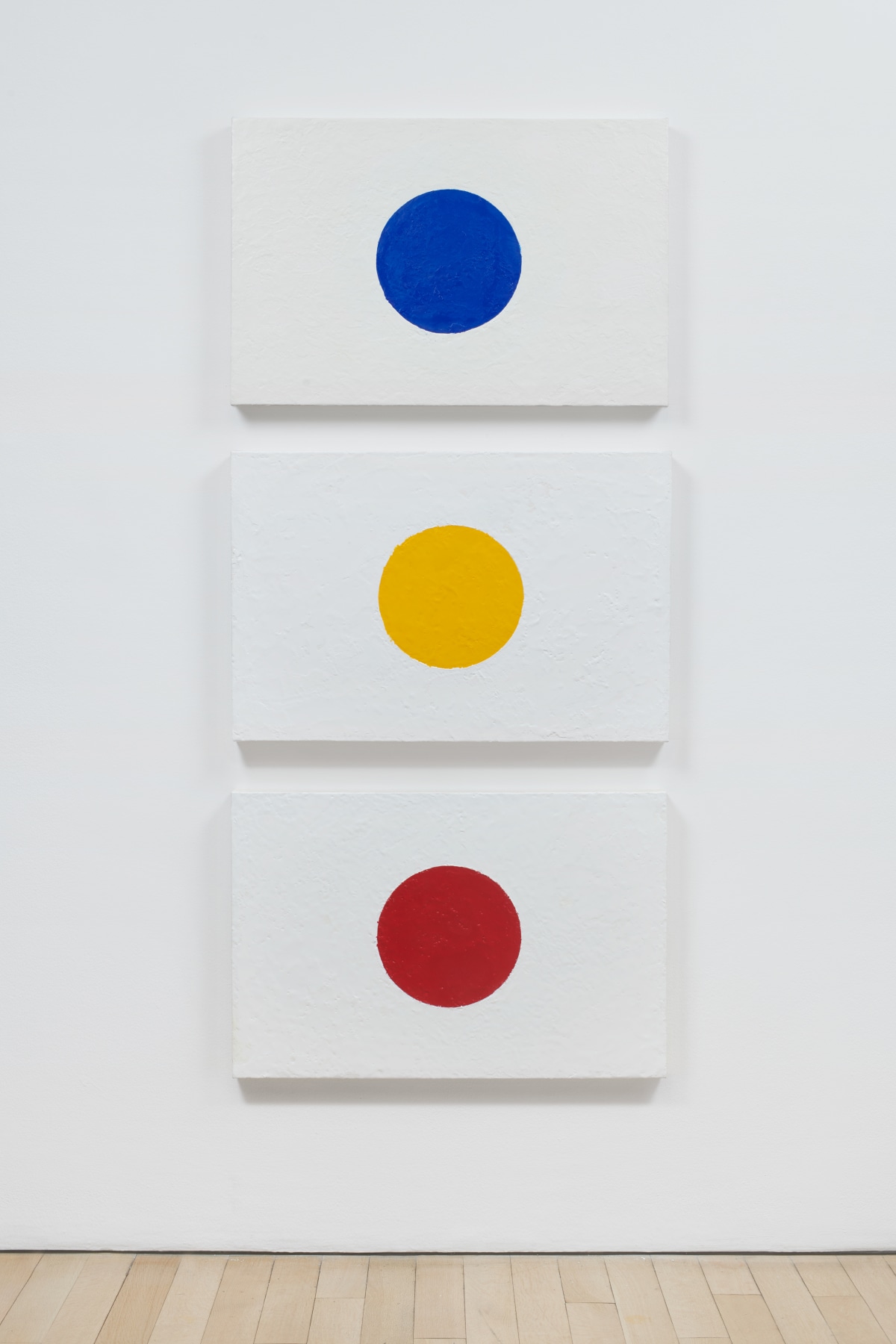 Three white canvases, each with a circle of a different primary color